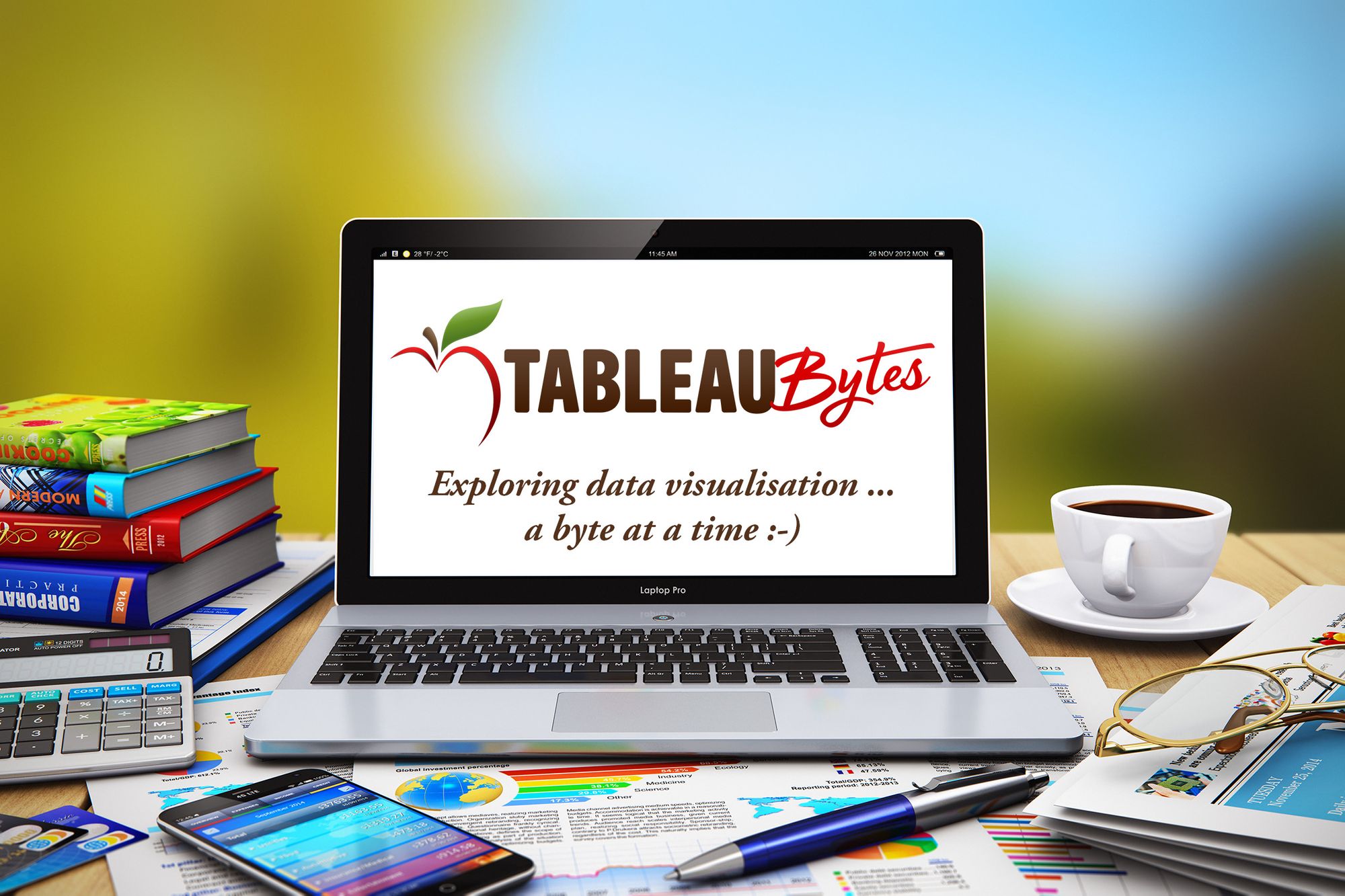 A laptop on a table surrounded by books and items on a desk. The laptop has the TableauBytes logo displayed on the screen.